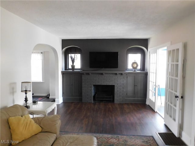 living room with french doors, a textured ceiling, a brick fireplace, and dark wood-type flooring