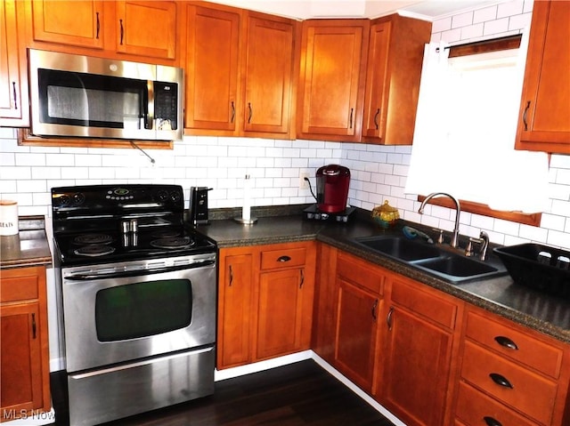 kitchen featuring dark stone counters, sink, dark hardwood / wood-style floors, decorative backsplash, and stainless steel appliances