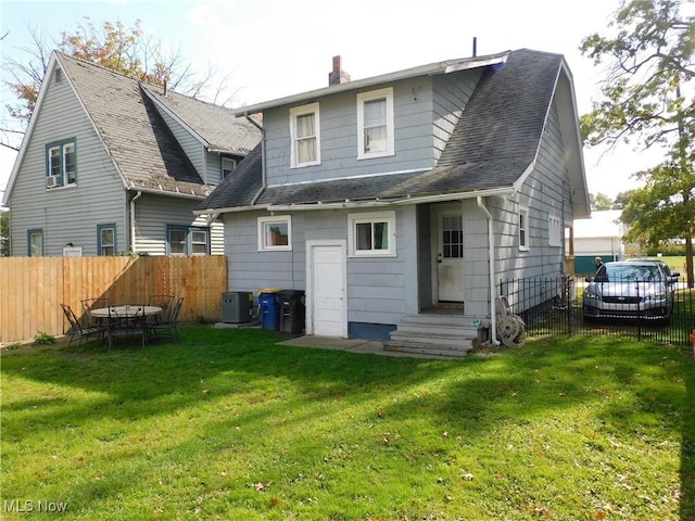 rear view of house featuring cooling unit and a lawn