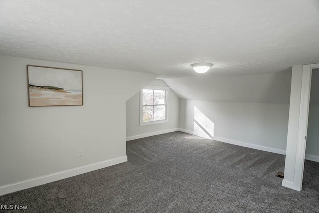 bonus room featuring a textured ceiling, lofted ceiling, and dark colored carpet