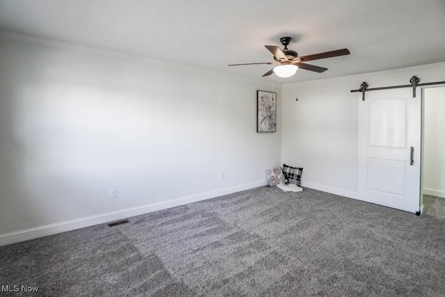 unfurnished bedroom with a barn door, dark carpet, ceiling fan, and ornamental molding