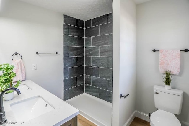 bathroom with a tile shower, vanity, and toilet