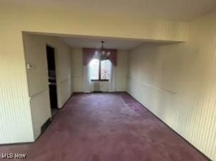 carpeted spare room with an inviting chandelier