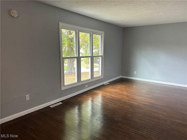 empty room with dark hardwood / wood-style flooring and a textured ceiling