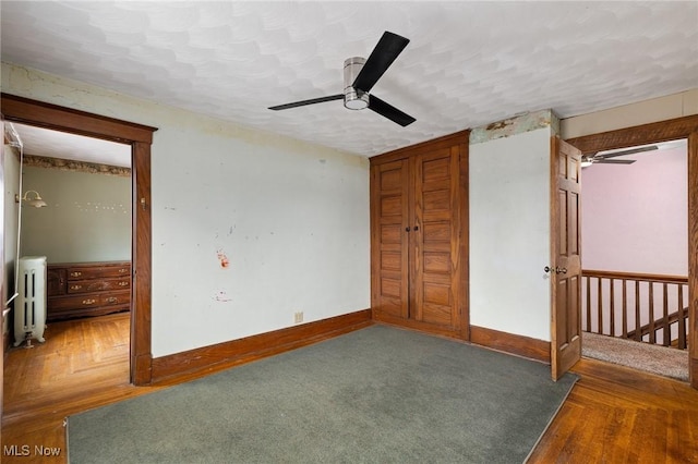 unfurnished bedroom with dark hardwood / wood-style flooring, ceiling fan, and radiator heating unit