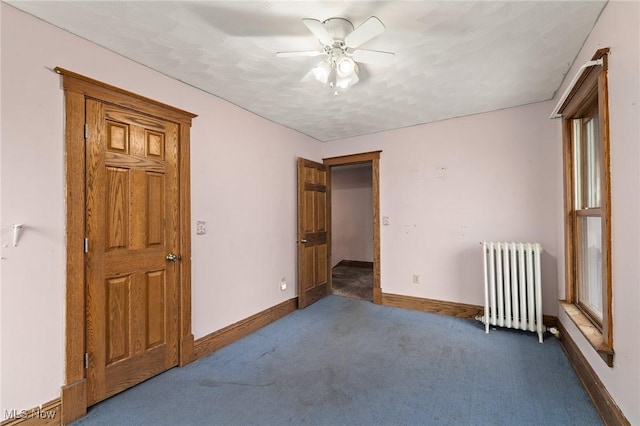 unfurnished bedroom featuring radiator, ceiling fan, and dark carpet