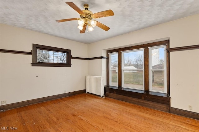 unfurnished room with radiator heating unit, light wood-type flooring, and ceiling fan