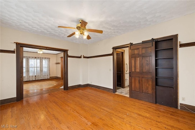 spare room with a barn door, ceiling fan, hardwood / wood-style floors, and a textured ceiling