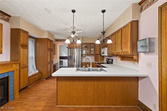 kitchen featuring a tile fireplace, sink, light wood-type flooring, appliances with stainless steel finishes, and kitchen peninsula