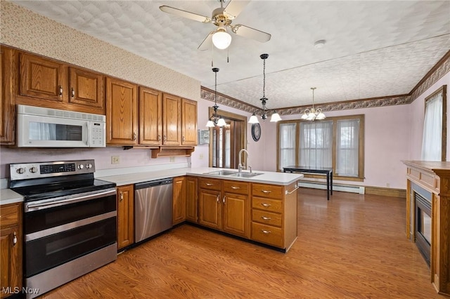 kitchen with sink, light hardwood / wood-style flooring, kitchen peninsula, decorative light fixtures, and appliances with stainless steel finishes