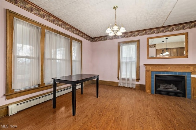 dining area with a chandelier, ornamental molding, baseboard heating, wood-type flooring, and a tiled fireplace