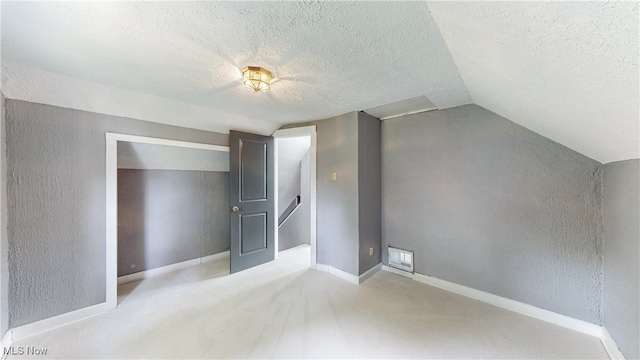 additional living space featuring a textured ceiling, light colored carpet, and lofted ceiling