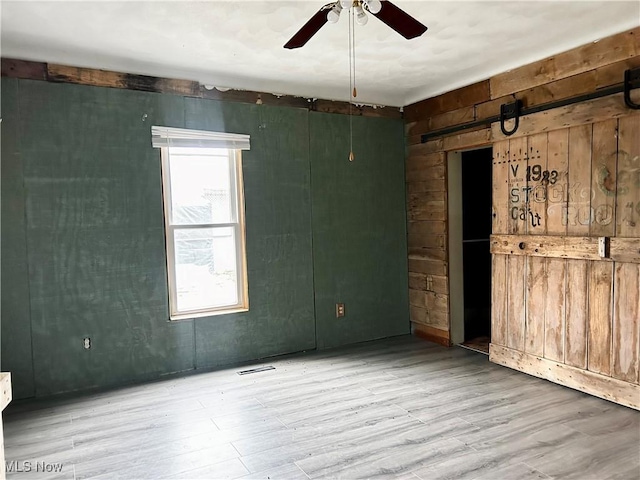 spare room with wood walls, ceiling fan, a barn door, and light wood-type flooring