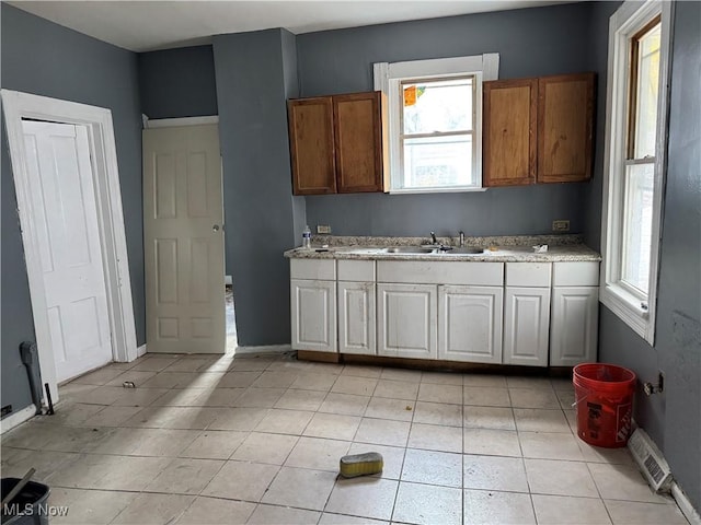 kitchen with light tile patterned floors, white cabinetry, a healthy amount of sunlight, and sink