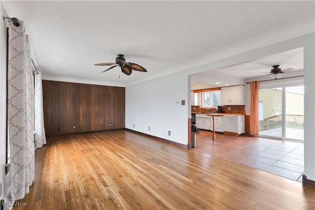 unfurnished living room with built in desk, light hardwood / wood-style flooring, and ceiling fan