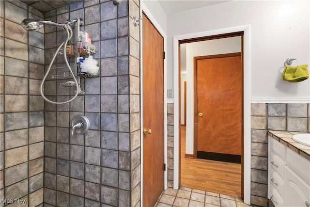 bathroom with hardwood / wood-style floors, vanity, a tile shower, and tile walls