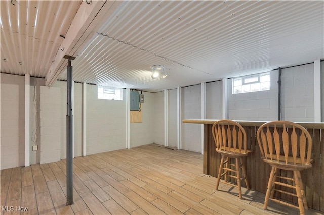 basement featuring bar area, electric panel, and light hardwood / wood-style flooring