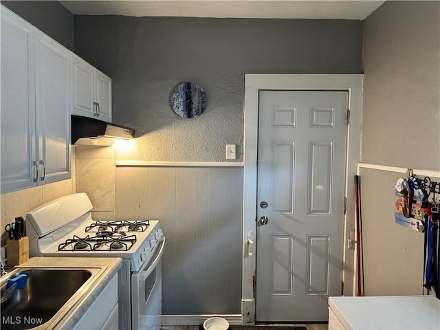 kitchen with under cabinet range hood, light countertops, white range with gas cooktop, wainscoting, and a sink