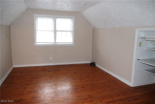 bonus room with a textured ceiling, vaulted ceiling, and dark wood-type flooring