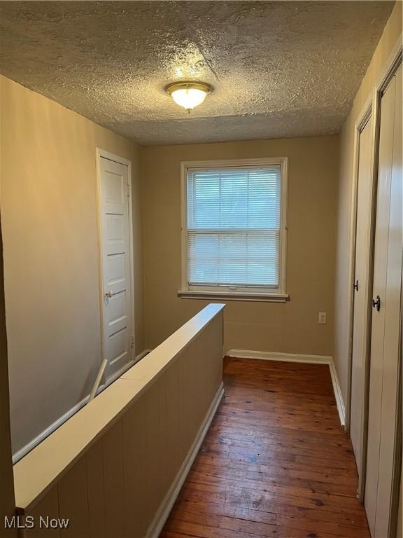 corridor with a textured ceiling and dark hardwood / wood-style floors