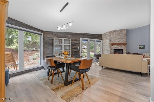 dining area with a stone fireplace, light hardwood / wood-style floors, and lofted ceiling