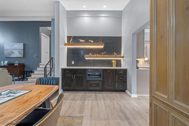 kitchen with backsplash, dark brown cabinetry, oven, and light hardwood / wood-style floors