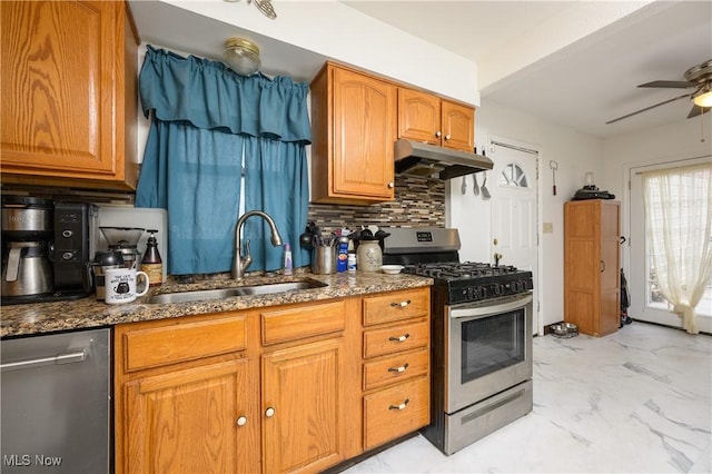 kitchen with appliances with stainless steel finishes, backsplash, ceiling fan, sink, and dark stone countertops