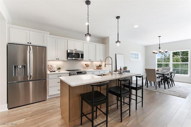 583 Iris Pl, Aurora, OH 44202 - kitchen featuring appliances with stainless steel finishes, a sink, light wood-style floors, an island with sink, and backsplash