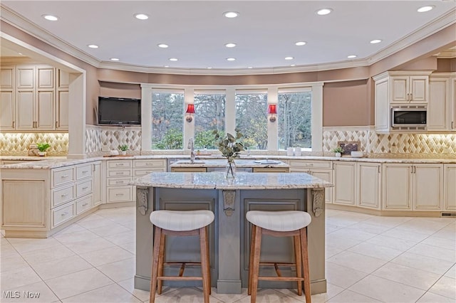 kitchen with a breakfast bar, cream cabinets, stainless steel microwave, and light stone countertops