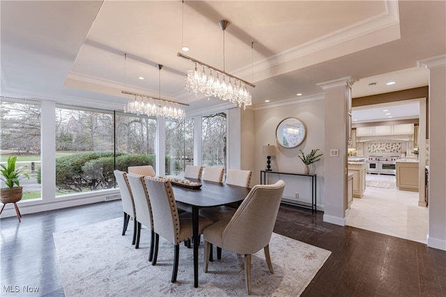 dining area featuring a tray ceiling, a chandelier, light hardwood / wood-style floors, and ornamental molding