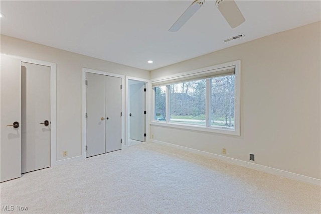 unfurnished bedroom featuring ceiling fan, light colored carpet, and multiple closets