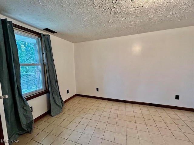 spare room with a textured ceiling and light tile patterned flooring