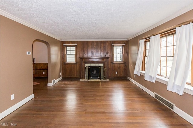 unfurnished living room featuring a tile fireplace, crown molding, wooden walls, and dark wood-type flooring