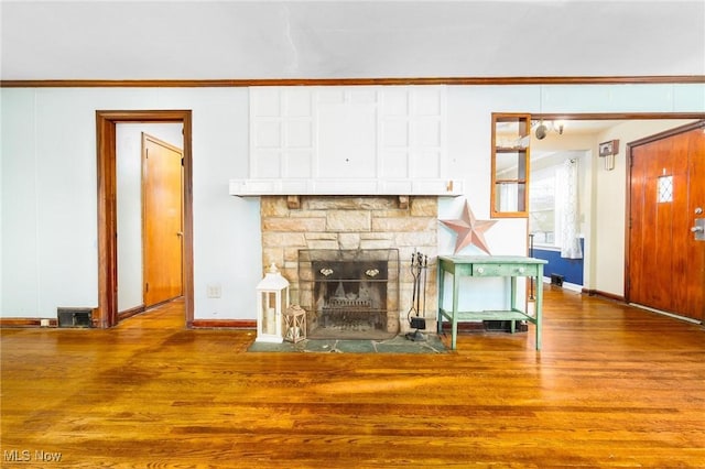 unfurnished living room featuring hardwood / wood-style flooring, a stone fireplace, and crown molding