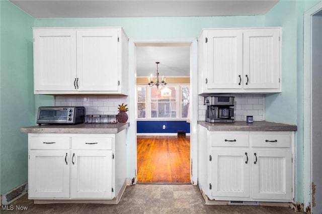 kitchen with white cabinets, backsplash, and a chandelier