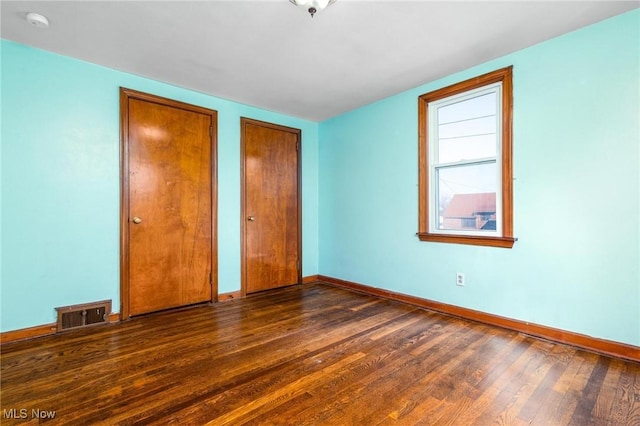 unfurnished bedroom featuring multiple closets and dark hardwood / wood-style floors