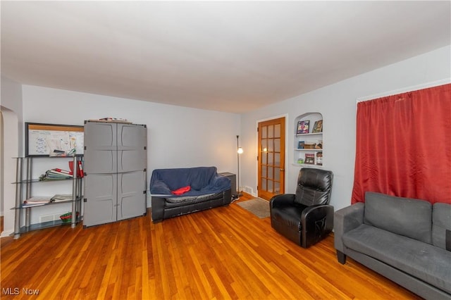 living area with built in shelves, french doors, and wood-type flooring