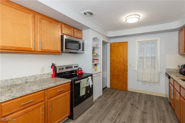 kitchen featuring hardwood / wood-style flooring, light stone countertops, backsplash, and appliances with stainless steel finishes