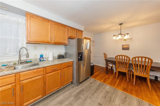 kitchen with backsplash, sink, light hardwood / wood-style flooring, stainless steel fridge, and a notable chandelier