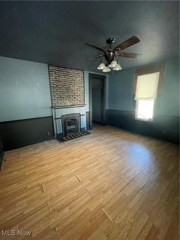 unfurnished living room featuring ceiling fan, light hardwood / wood-style floors, and a wood stove