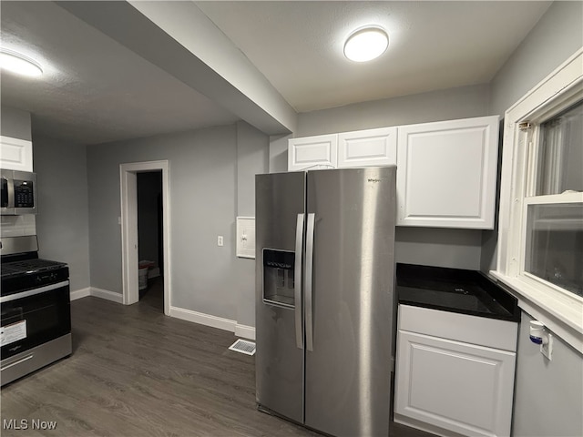 kitchen with dark wood-type flooring, appliances with stainless steel finishes, and white cabinetry