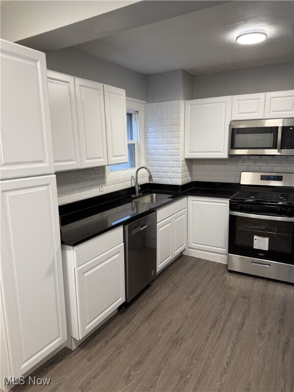 kitchen featuring white cabinets, dark hardwood / wood-style flooring, stainless steel appliances, sink, and backsplash