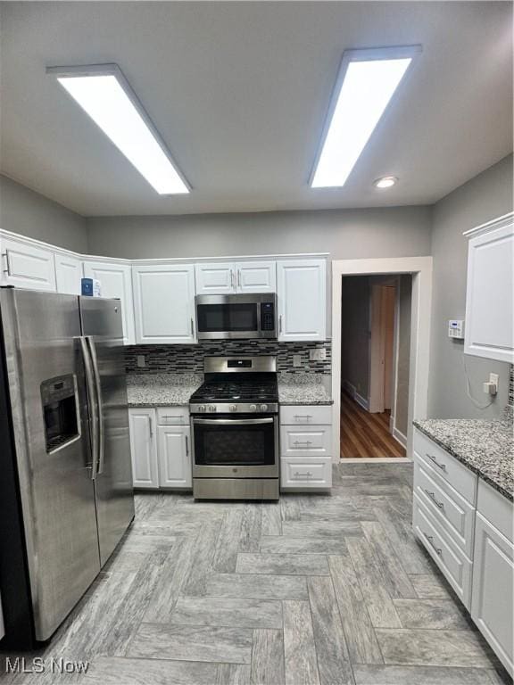 kitchen featuring backsplash, white cabinets, light wood-type flooring, light stone countertops, and appliances with stainless steel finishes