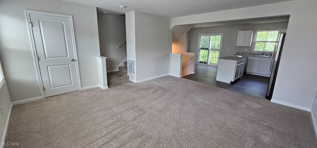 unfurnished living room featuring sink, dark carpet, and a textured ceiling