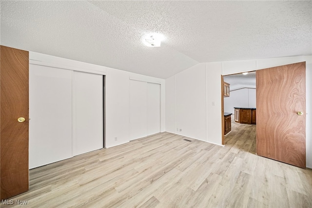 interior space with vaulted ceiling, two closets, a textured ceiling, and light wood-type flooring