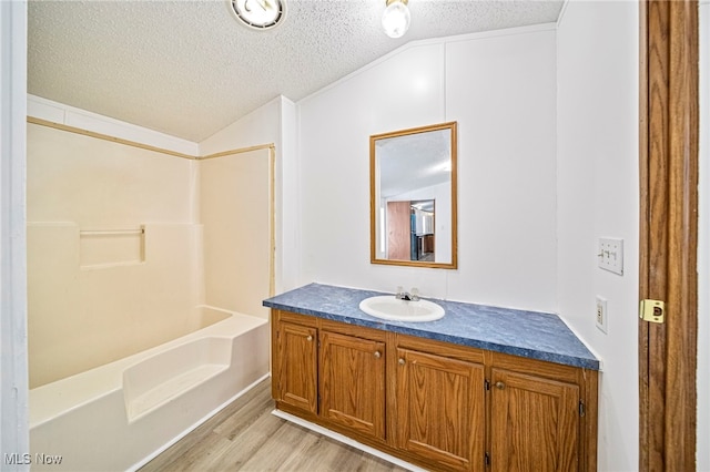 bathroom featuring lofted ceiling, a textured ceiling, shower / bathtub combination, vanity, and hardwood / wood-style floors