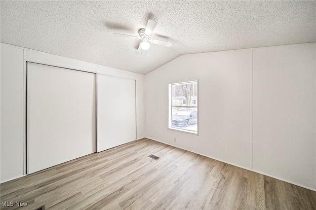 unfurnished bedroom with lofted ceiling, a textured ceiling, a closet, ceiling fan, and light hardwood / wood-style floors