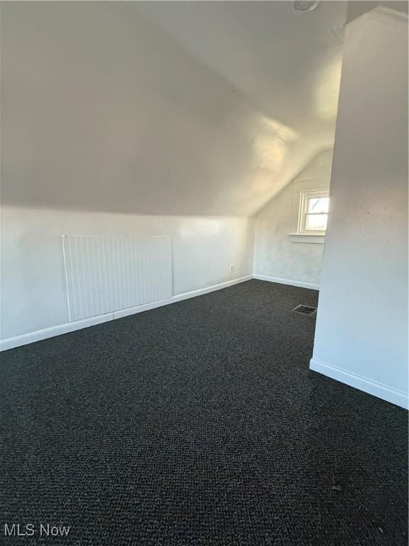 additional living space featuring dark carpet and lofted ceiling