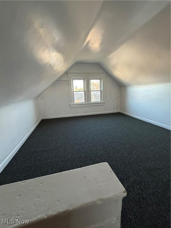 additional living space featuring vaulted ceiling and dark carpet