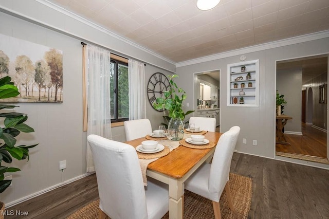 dining room with built in shelves, ornamental molding, and dark wood-type flooring